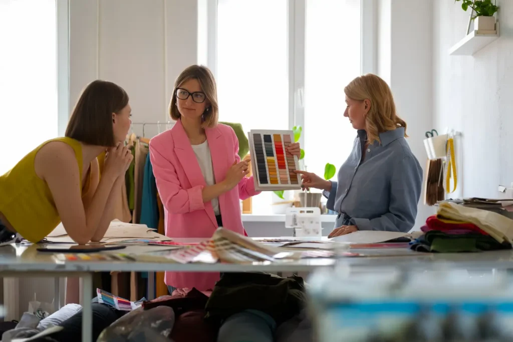 Dona de confecção colaborando com duas clientes para escolher as cores das peças, uma das formas de crowdsourcing.