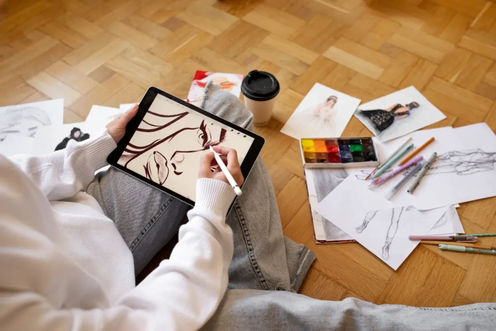 Designer criando ilustração de moda com um tablet, com desenhos manuais no chão