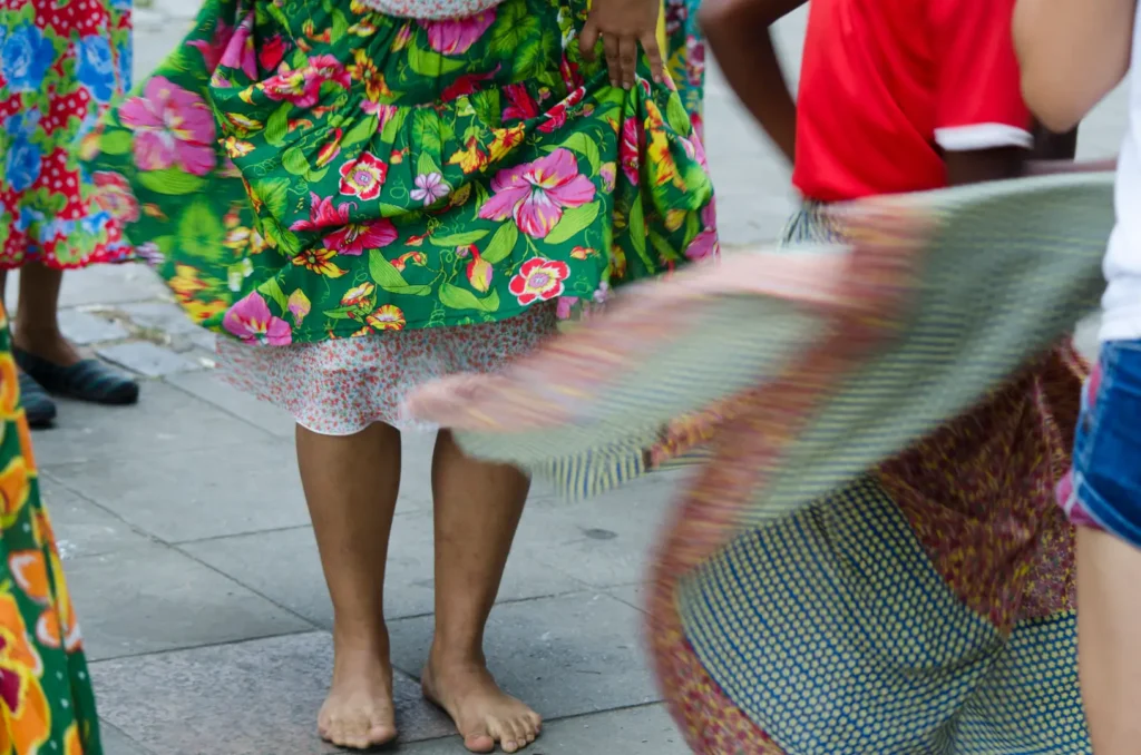 Mulheres dançando na rua, usando saias floridas de diferentes cores, feitas com tecido chita