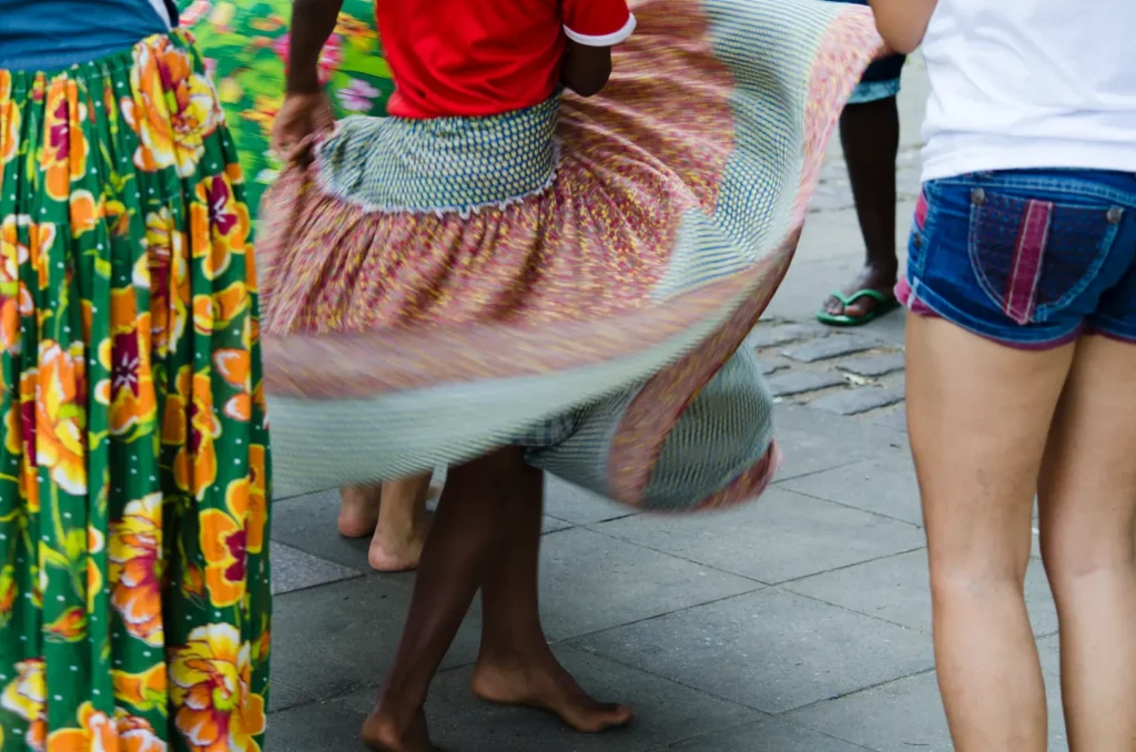 Mulher dançando na rua usando uma saia de festa junina, com estampa florida e de poá, feita com tecido chita