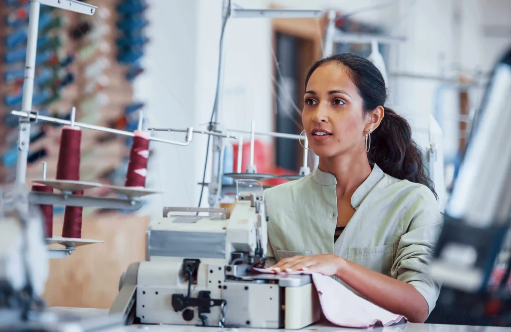 Indústria confecção: mulher costurando em máquina industrial.