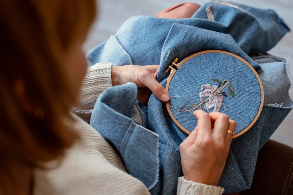 Estilista adicionando bordado livre, um dos vários tipos de bordados, a uma peça jeans