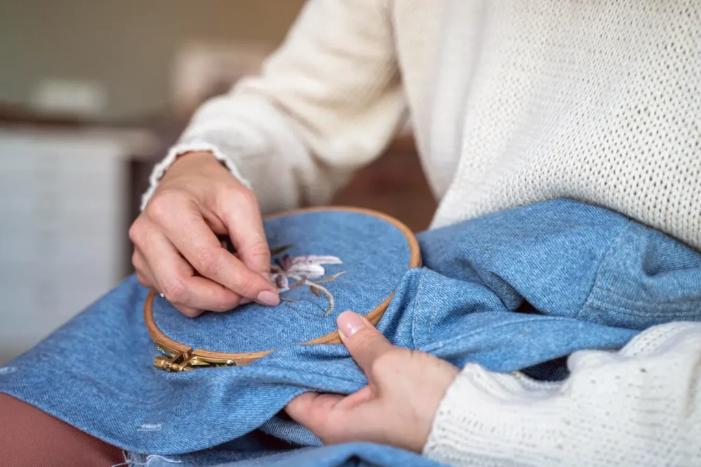 Estilista bordando bordado livre em uma peça jeans