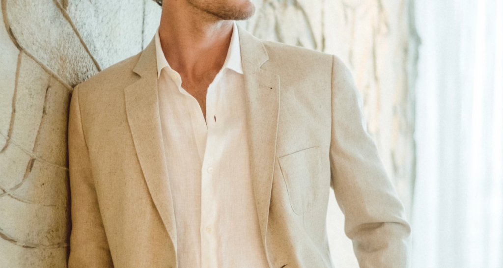 The image shows a man posing in a neutral-colored linen suit.