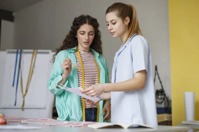 Designing clothes: Two women analyzing a technical drawing for fashion creation.