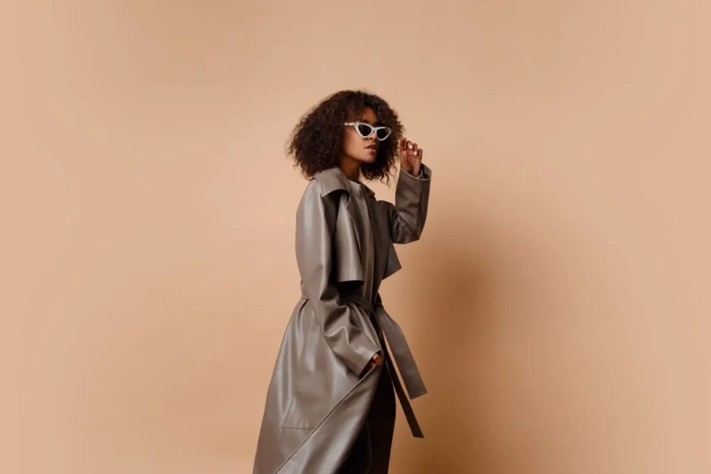 Modelo posando com um trenchcoat de couro e um óculos escuro de armação branca