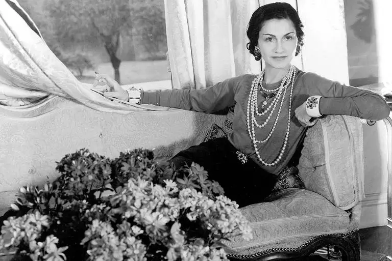 Coco Chanel sentada em um sofá. Ela foi e continua sendo uma das mulheres mais influentes na moda.