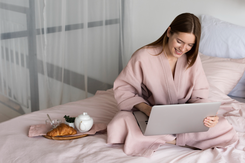 Mulher vestindo homewear e mexendo no notebook, em sua cama.