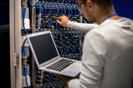 Man working with a supercomputer connecting server cables and checking data on the laptop.