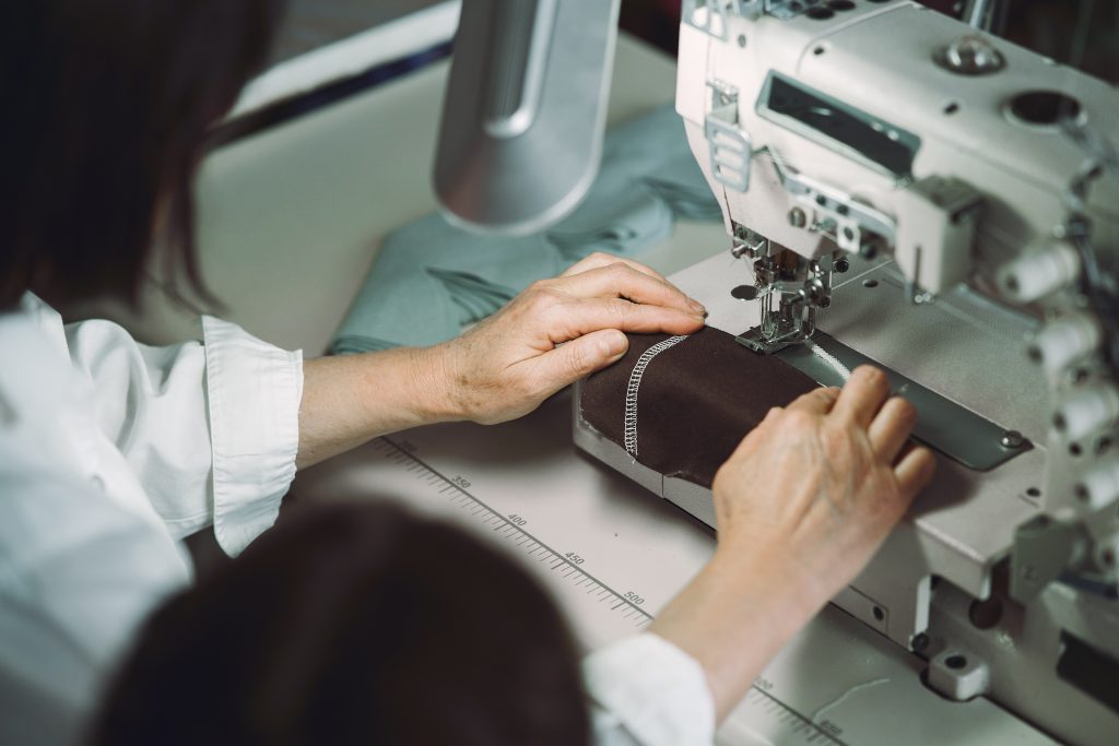 The image shows in detail the hands of a professional working with a sewing machine in the context of Industry 5.0.