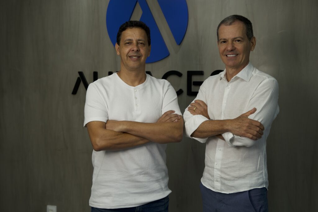 Ricardo Cunha y Claudio Grando, Fundadores de Audaces sonriendo con el logo de empresa al fondo