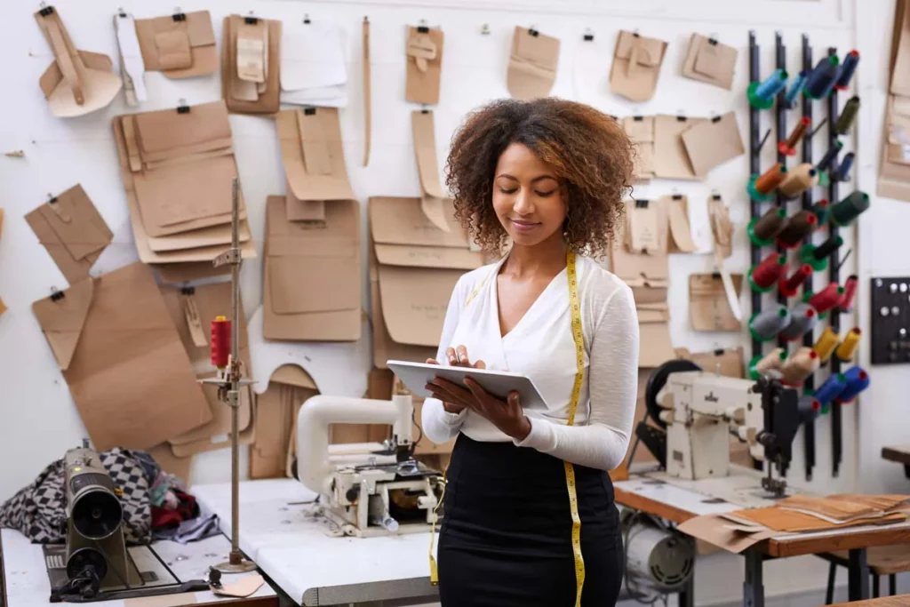 Woman in a fashion atelier checking macro trends on a tablet for the next collection.