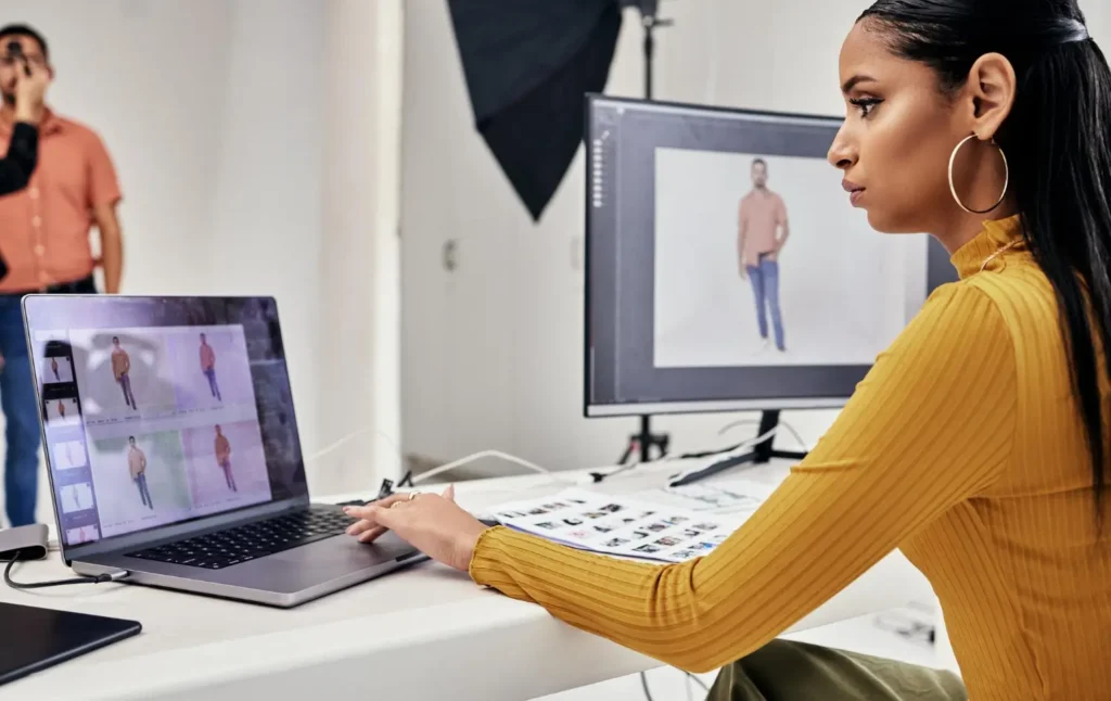 Estilista supervisionando um ensaio fotográfico de moda, olhando para as fotos do modelo em um computador com duas telas