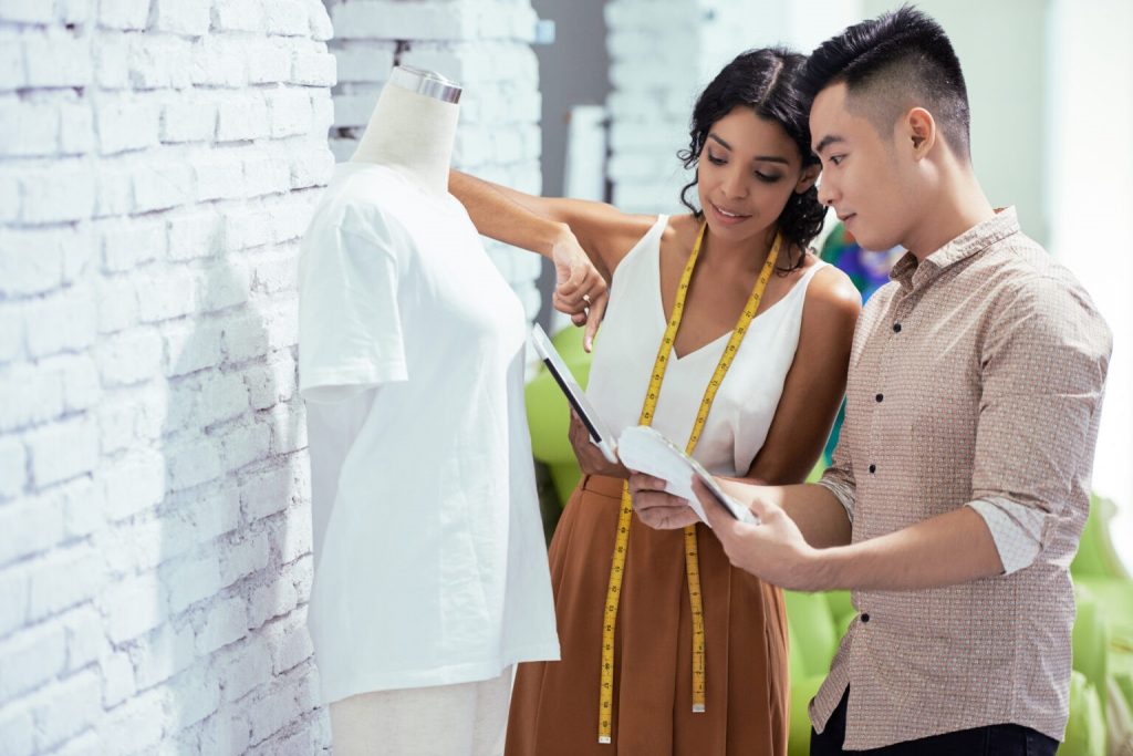 Designers de moda avaliando o controle de qualidade têxtil de uma nova coleção.