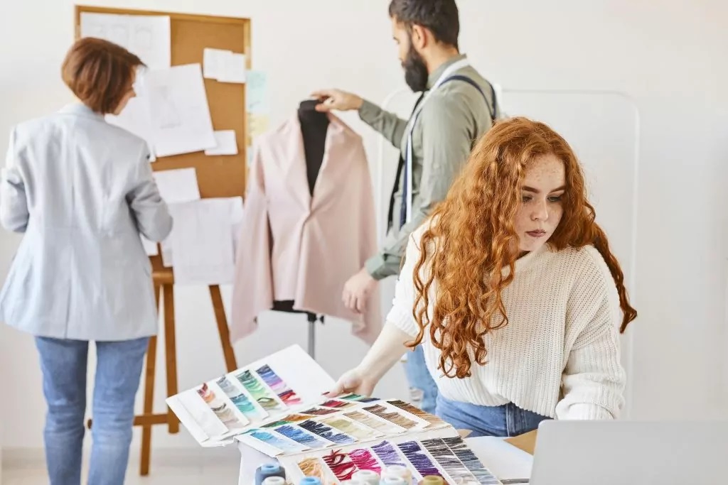 Two women and a man working in a fashion office to assess how to create a color chart for a clothing collection