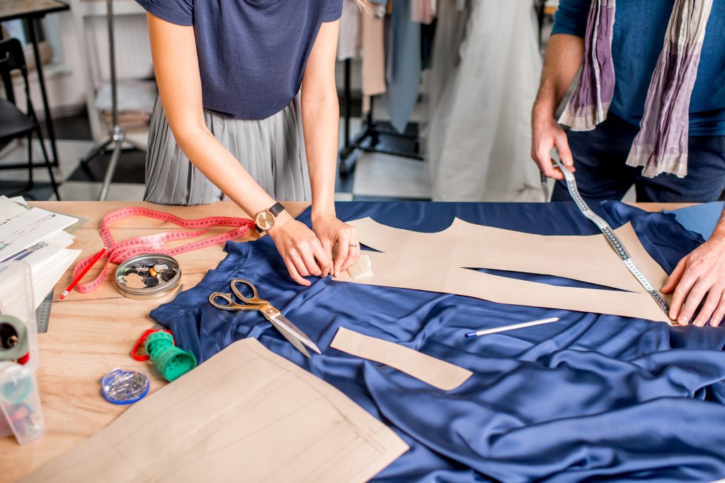 Diseñadoras cortando tela y confeccionando a mano una prenda de moda
