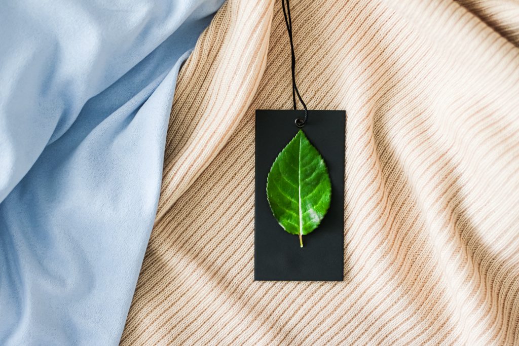 Fashion market: Green leaf on clothing tag and organic fabric background, sustainable fashion, and brand label concept.