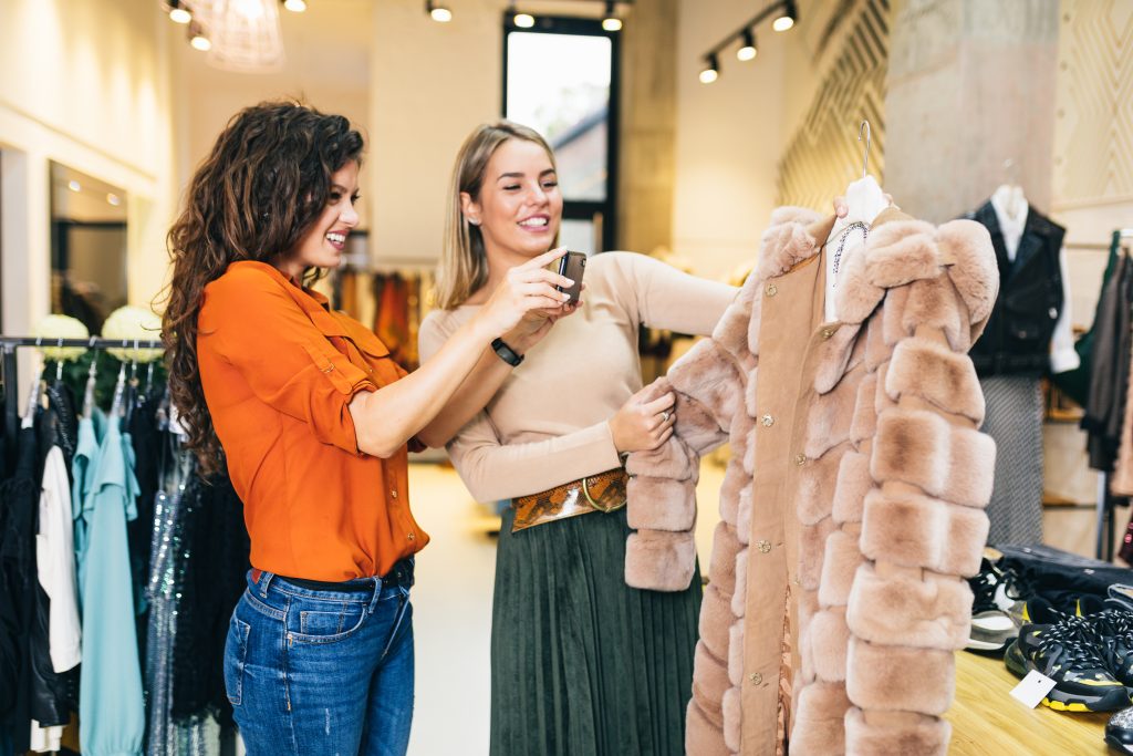 Sales pitch: Two female friends in a store taking pictures with a smartphone of an item of clothing.
