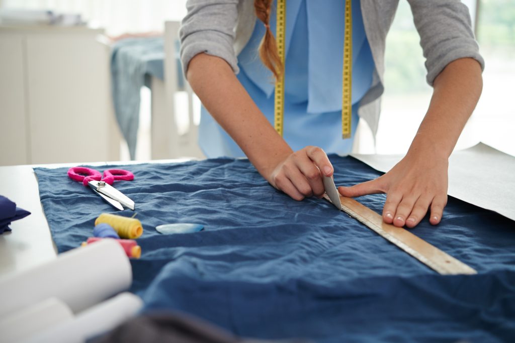 Woman working with a measuring tape in an atelier relying on the help of a pattern grading chart.