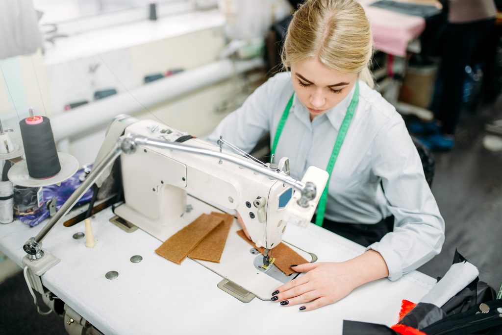 Moda circular: La imagen muestra a una mujer trabajando con una máquina de coser en un taller de moda.