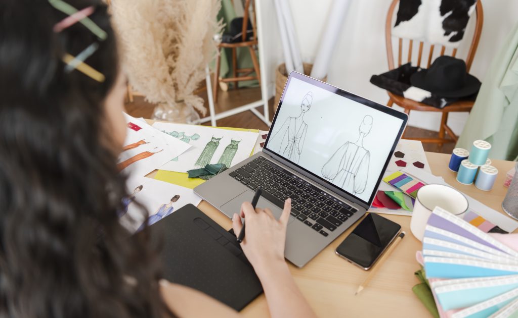 Digital sewing patterns: Female fashion designer drawing sketches for new collection on computer laptop.