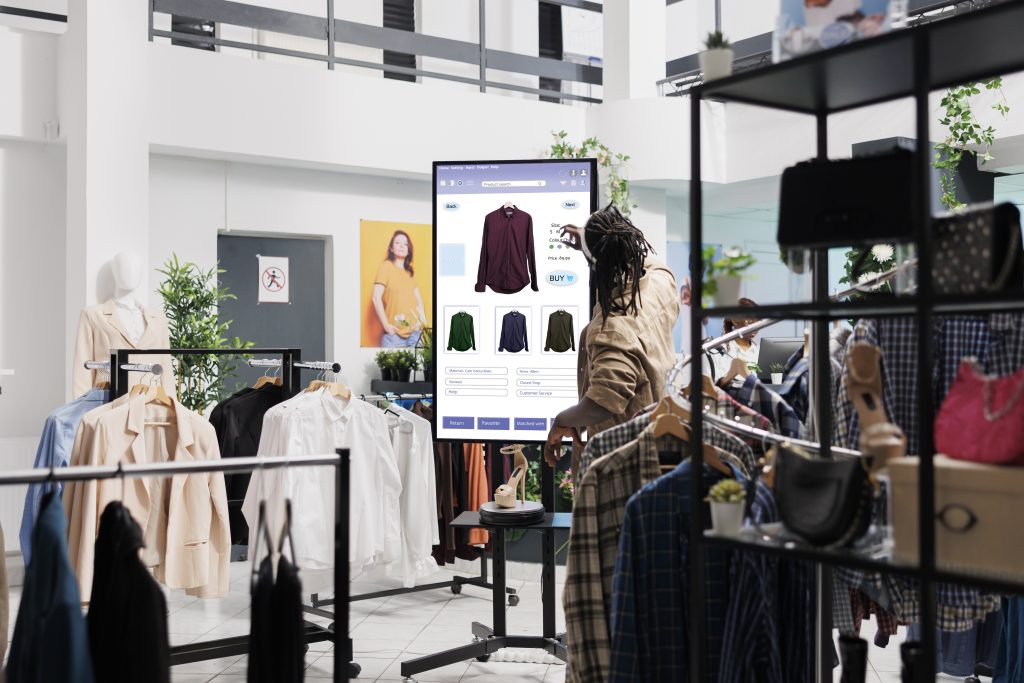 Phygital fashion: Woman in a physical clothing store using a virtual fitting room to decide which size to buy.
