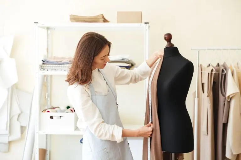 Fashion professional taking measurements of a sample garment directly on a mannequin.