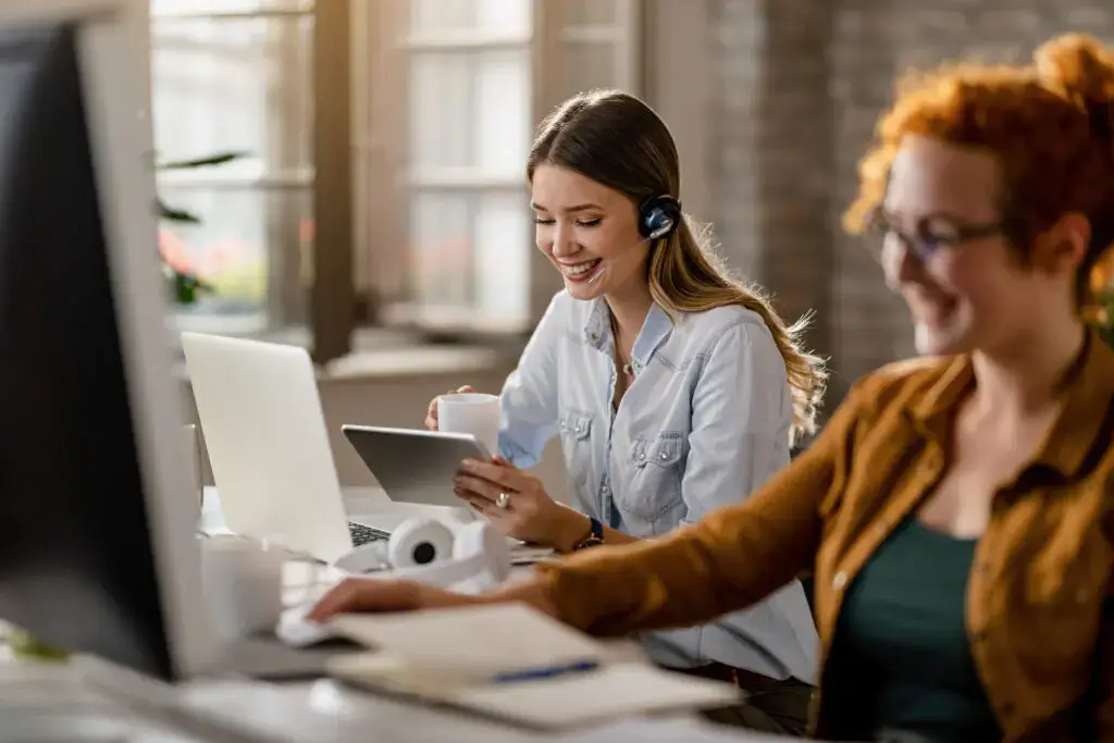 Online clothing business: Two women working in customer service smiling at the computer.