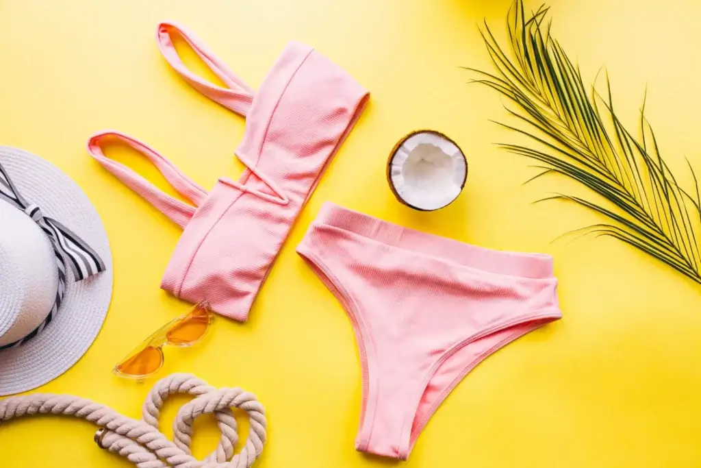 Online swimwear store: Pink bikini displayed on yellow background with sunglasses, hat, a sea rope and a green leaf.