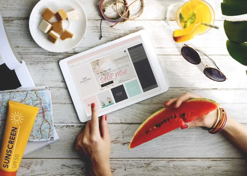 Online swimwear store: Woman shopping online in a summer mood, in a setting containing sunscreen, watermelon, sunglasses and orange juice.