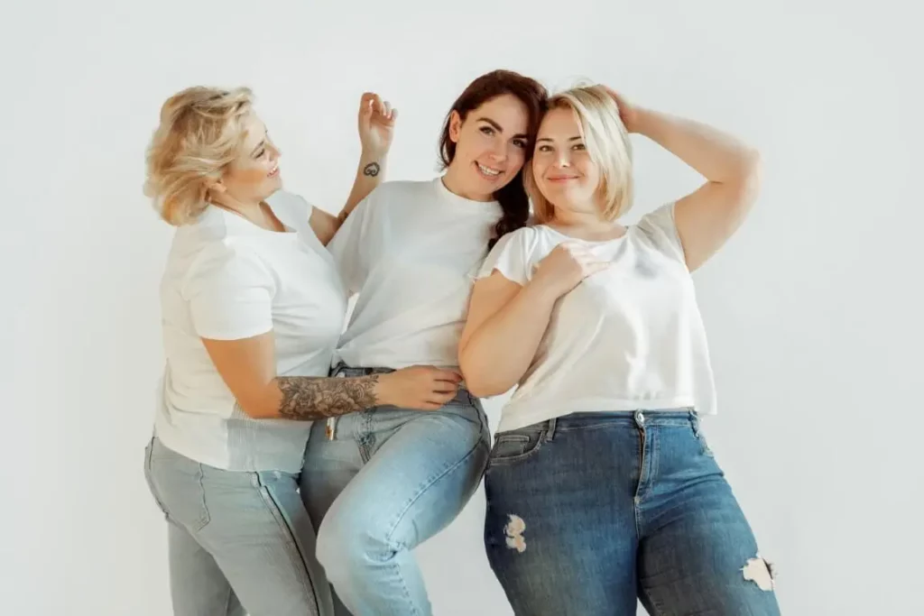 Plus-size fashion online: Three smiling women posing dressed in jeans and white t-shirt.
