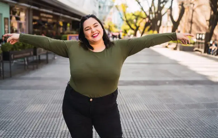 Plus-size fashion online: A young woman smiling standing outdoors on the street.