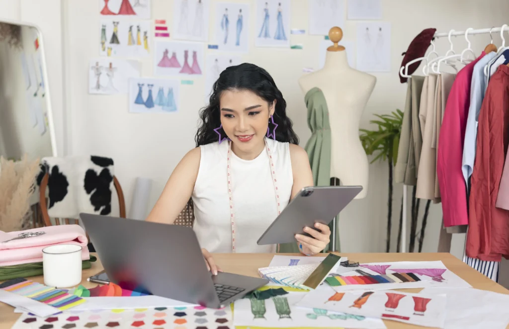 mulher criando molde de camisa em computador em ambiente com desenhos e peças de moda