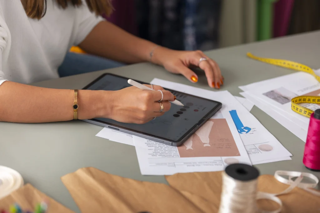 A woman designing on a tablet to optimize the process of making a clothing line