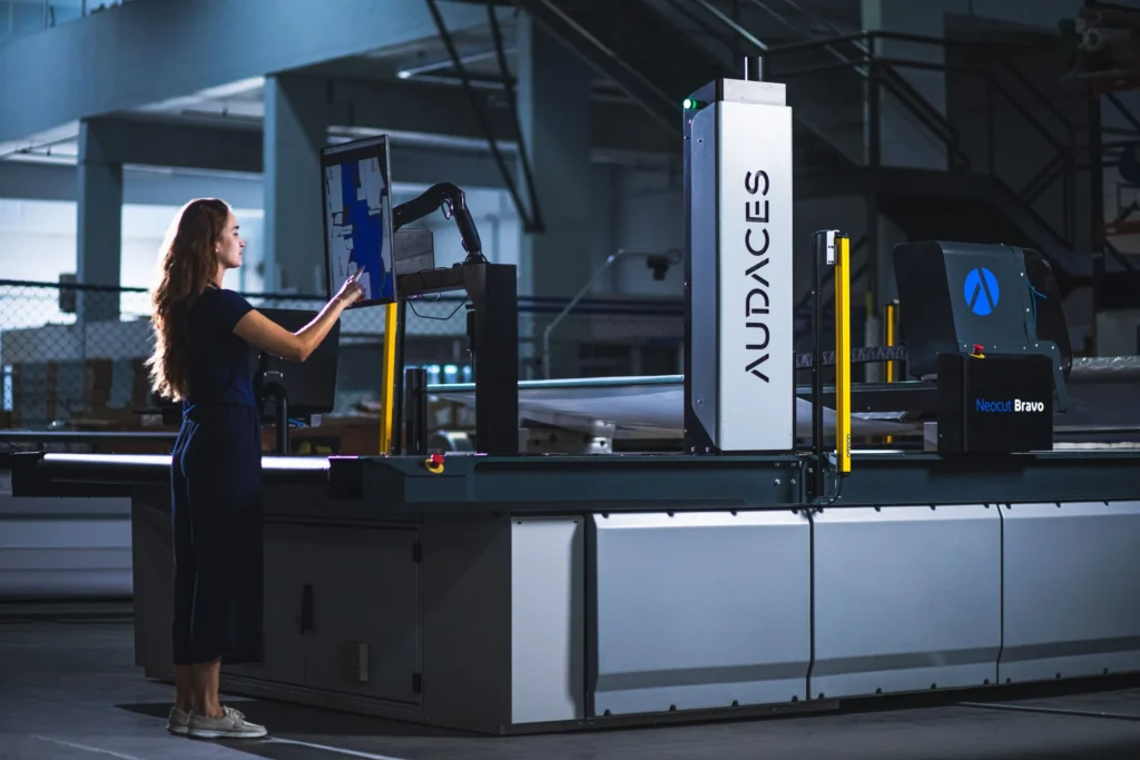 A female textile worker using a touch screen to operate an automatic fabric cutting machine.