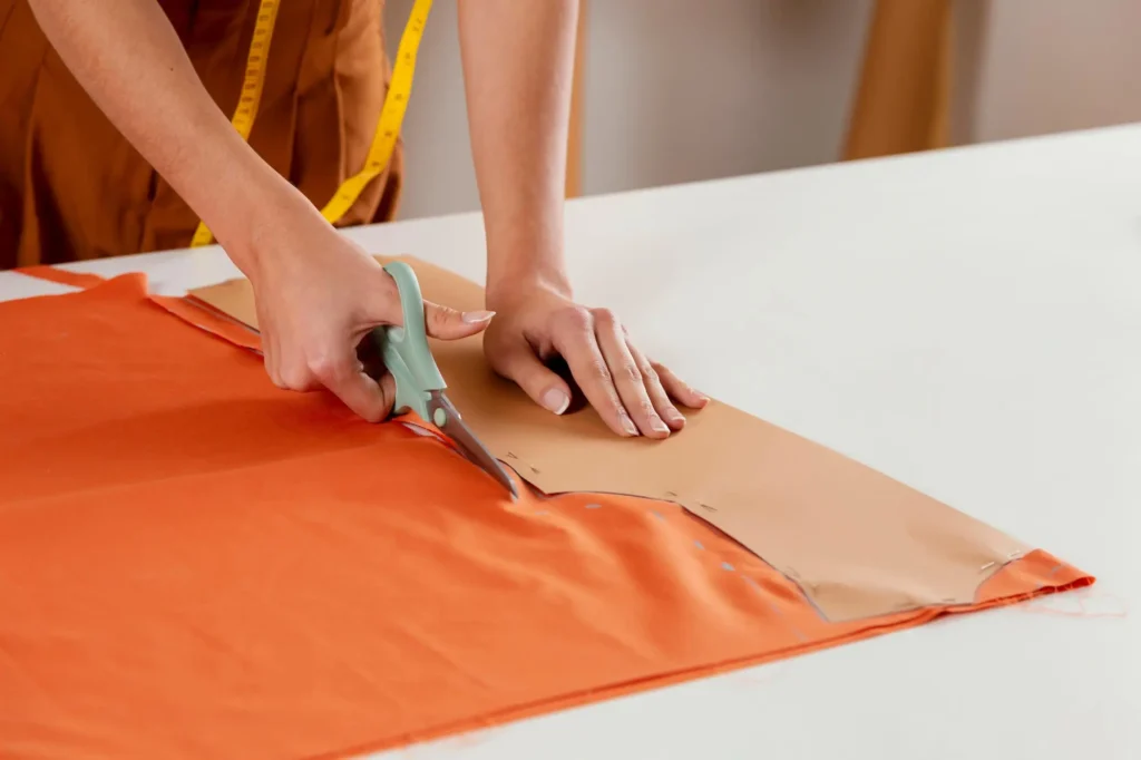 A fashion professional using a paper pattern of clothing to cut the fabric.