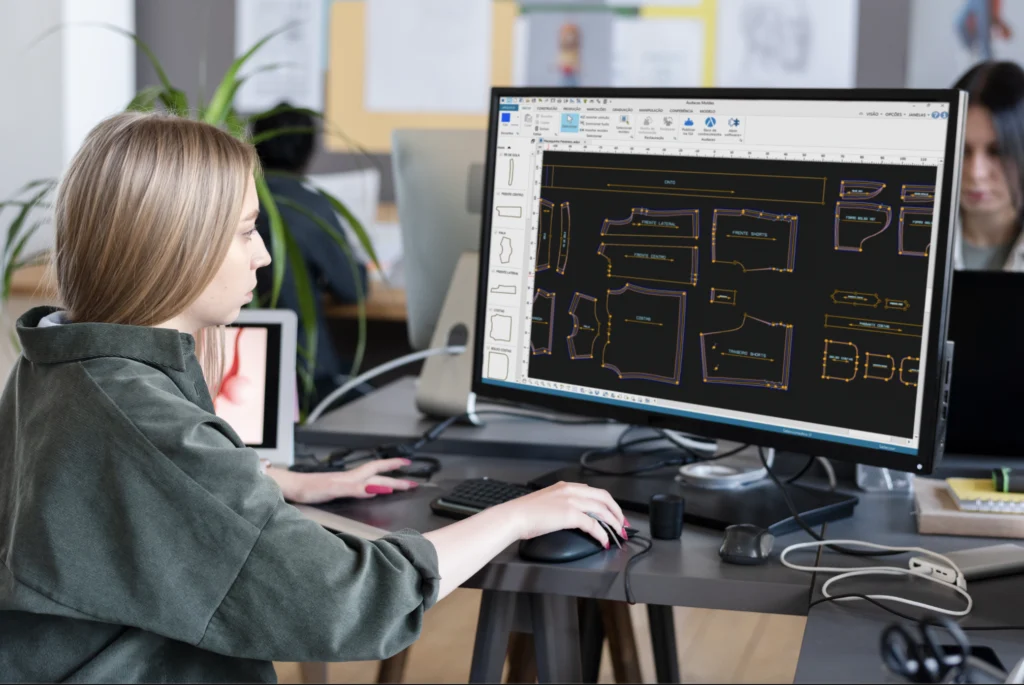 Mulher fazendo escala de tamanho de roupas no computador com Audaces Moldes.