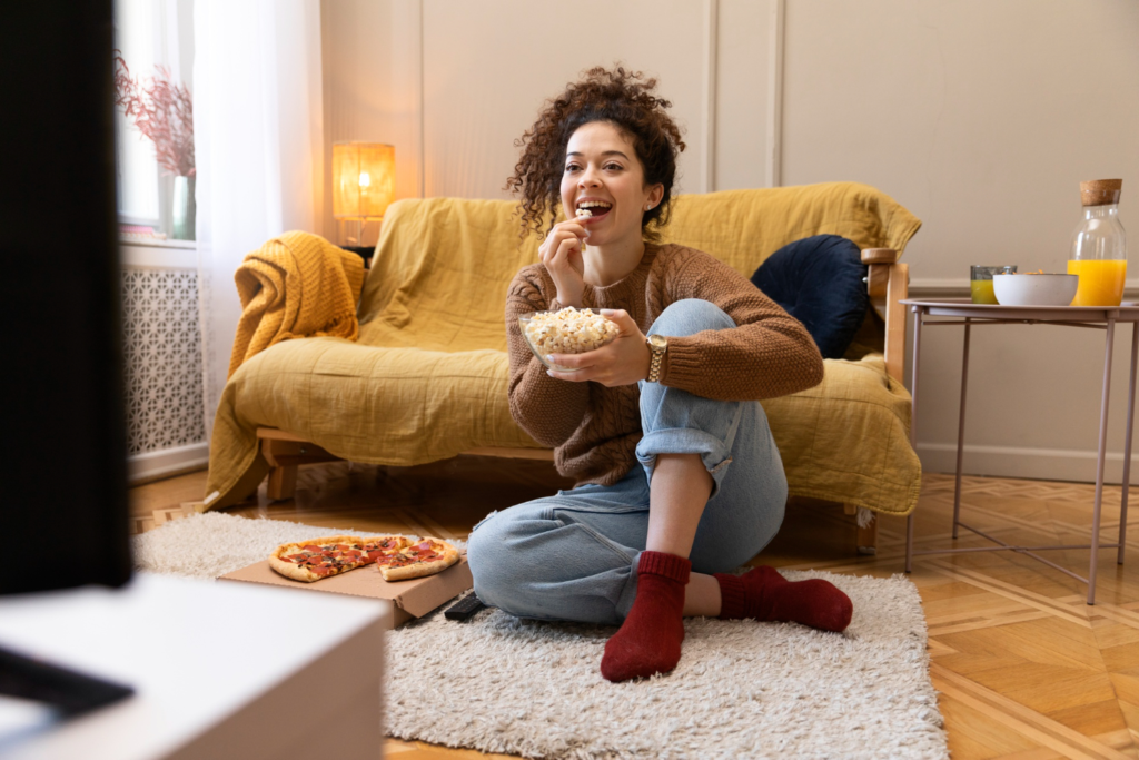 Mulher empolgada, comendo pipoca, enquanto assiste à TV.