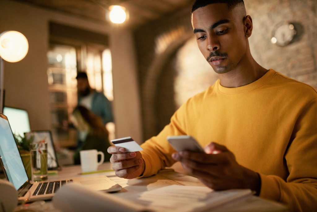 Homem mexe no celular segurando um cartão de crédito na outra mão.