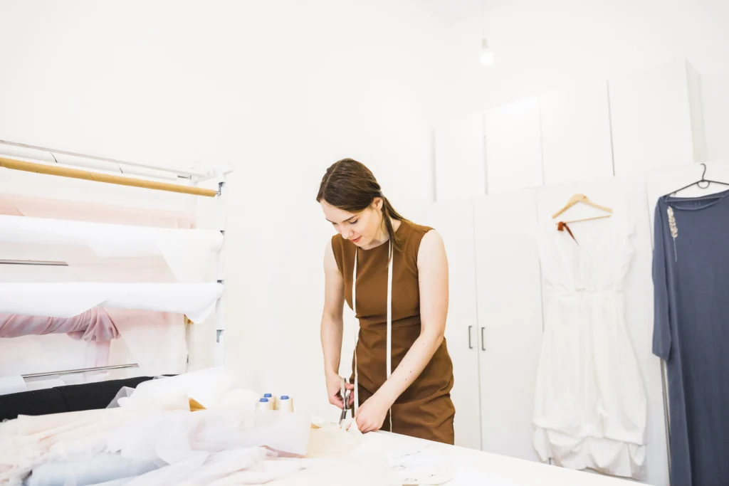 Diseñadora de moda cortando telas mientras revisa su plano de corte