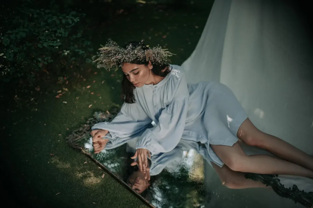 Mulher usando vestido azul claro fluido e uma coroa de flores em cenário etéreo. O fairycore é uma microtendência forte para 2026.