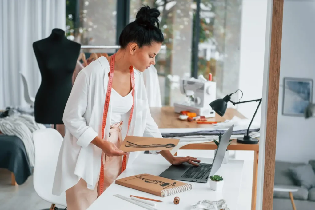 Estilista mexendo no computador em seu ateliê, com manequim no fundo