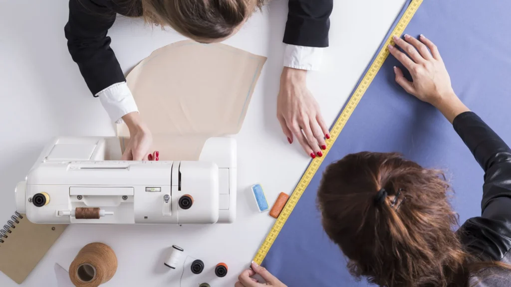 Producción industrial Argentina en acción: diseñadoras concentradas en el diseño de moda, rodeada de telas, herramientas y tecnología que impulsan la confección profesional en el país.