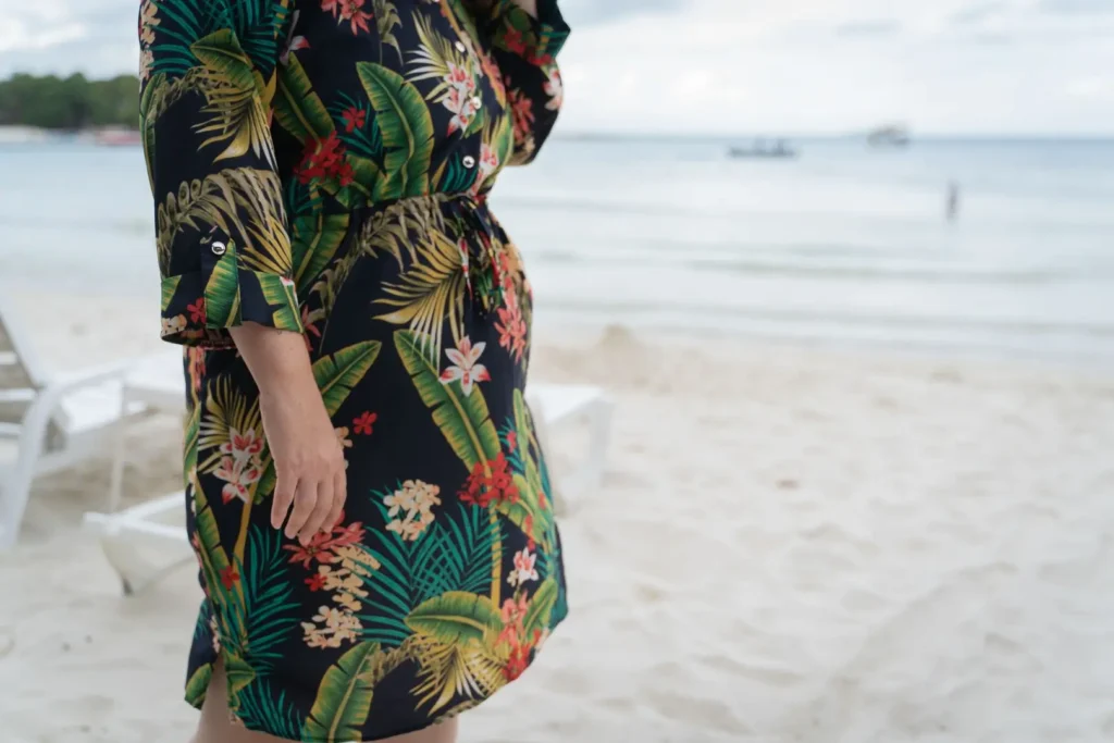 Mulher em uma praia com vestido de estampa tropical com flores e folhas