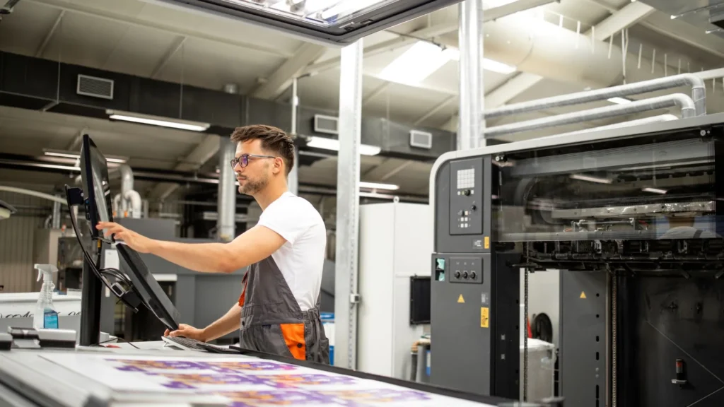 Una persona operando una máquina plotter industrial en un taller de confección, mostrando la precisión y tecnología aplicada en el corte de patrones para moda.