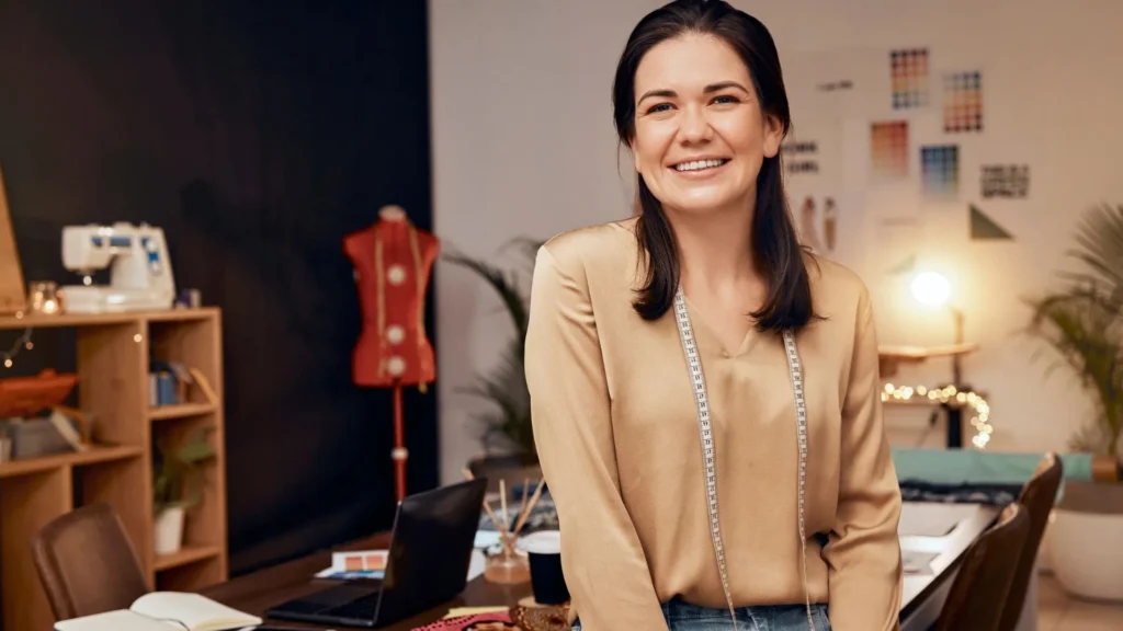 Una diseñadora de moda trabajando en el taller de una de las marcas de ropa argentinas más reconocidas, creando patrones y bocetos en una mesa llena de telas y herramientas de costura. El ambiente es creativo, con moodboards en las paredes y prendas colgadas como inspiración.