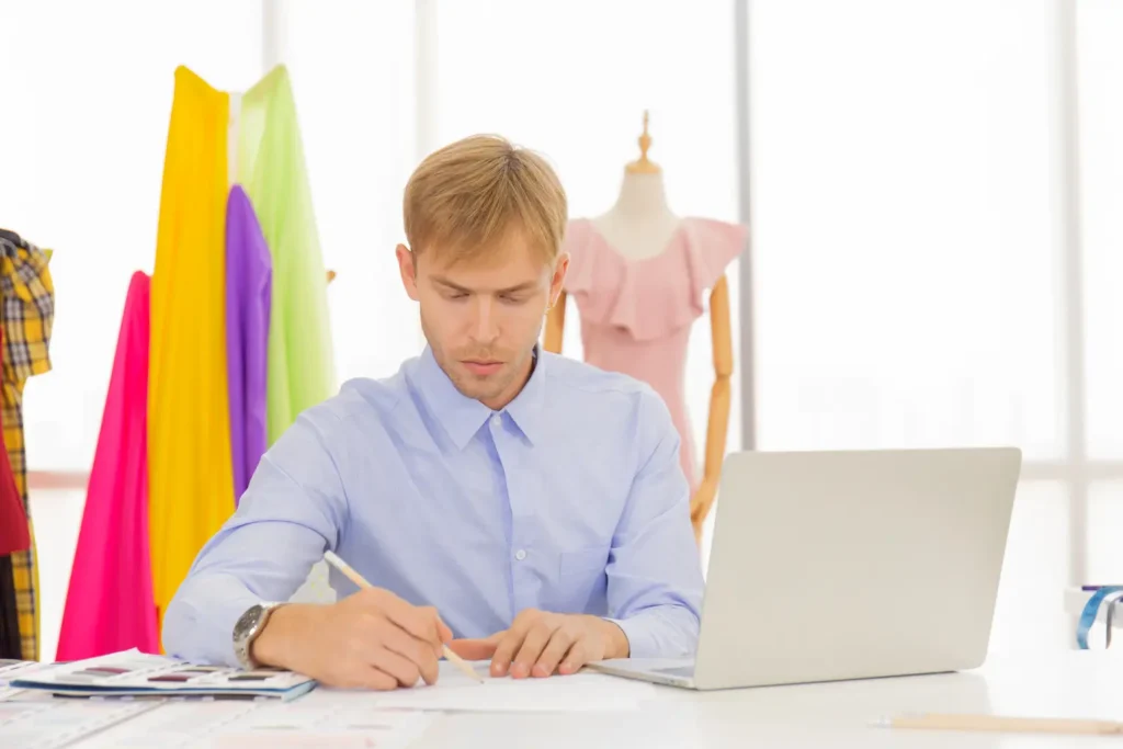 Um jovem estilista usando o notebook com software PLM em um ateliê de moda