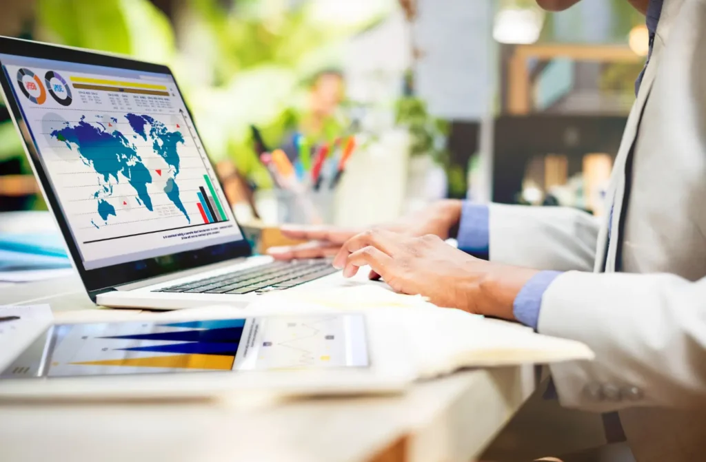 Pessoa mexendo em um notebook que mostra um mapa mundial espelhado e gráficos de resultados