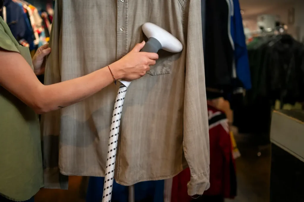 Persona usando una plancha a vapor para alisar una camisa abotonada en una tienda de ropa