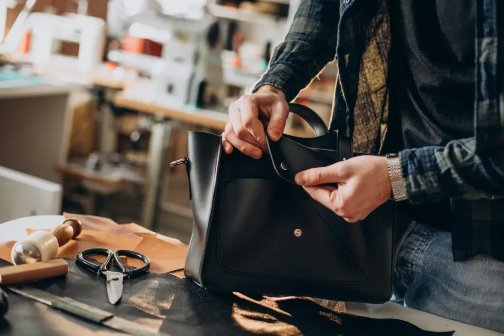 Designer de bolsas finalizando uma bolsa preta, no seu estúdio.